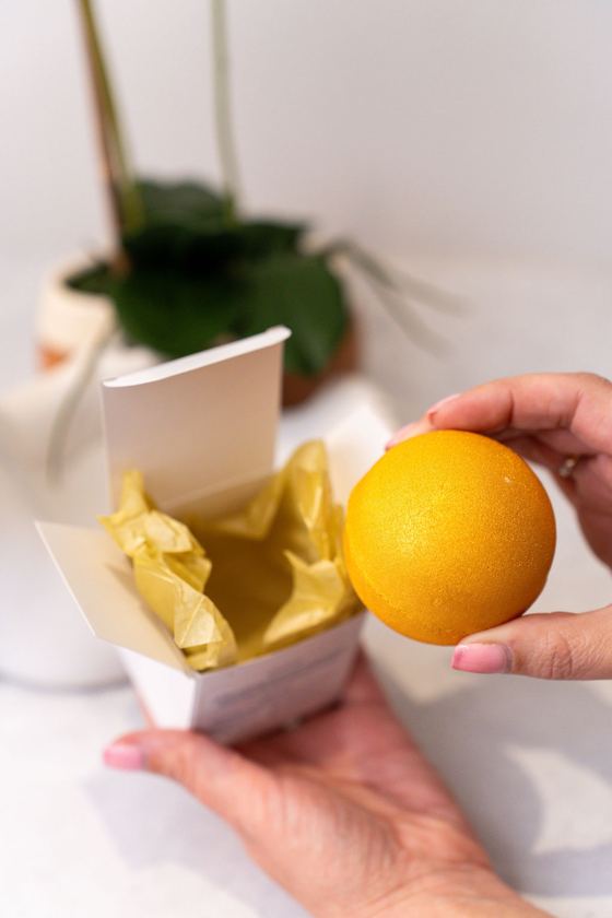 A golden bath bomb lifted from its gift box