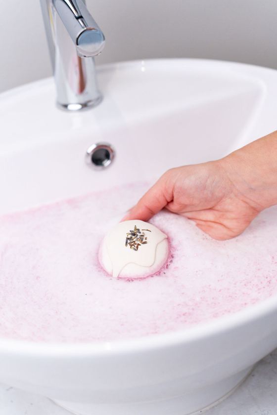 A bath bomb turning the water soft pink